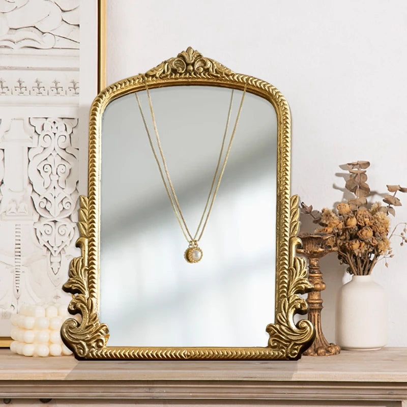 Miroir de coiffeuse doré — cadre en bois ancien - Nesty, miroir cintré doré à relief posé sur une étagère en bois, collier doré suspendu dessus, près de fleurs séchées