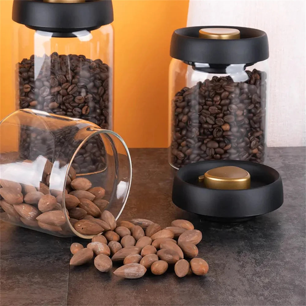 Boîte hermétique en verre pour café en grains Nesty, trois boîtes hermétiques en verre, deux remplies de grains de café et une renversée avec des amandes répandues, sur plan de travail sombre devant fond orange
