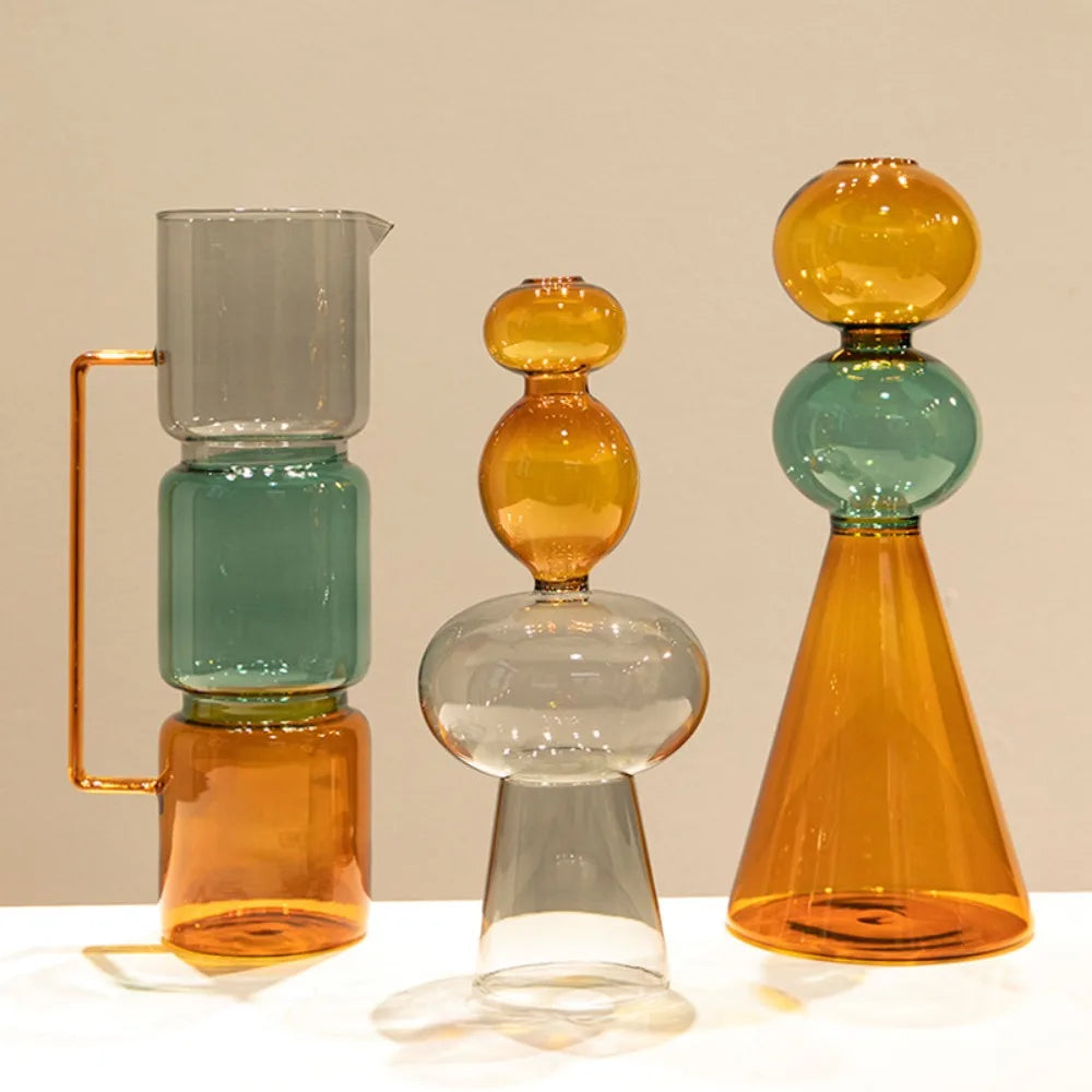 Vase en verre double paroi coloré, culture hydroponique - Nesty - Trois modèles empilés en verre gris, vert et ambré, formes bécher, boule et cône, sur une table blanche