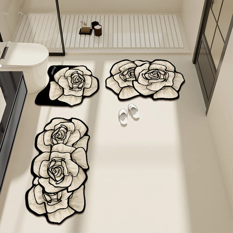 Set de trois tapis de salle de bain en forme de roses blanches à contour noir, vus d'en haut dans une salle de bain avec douche et radiateur.