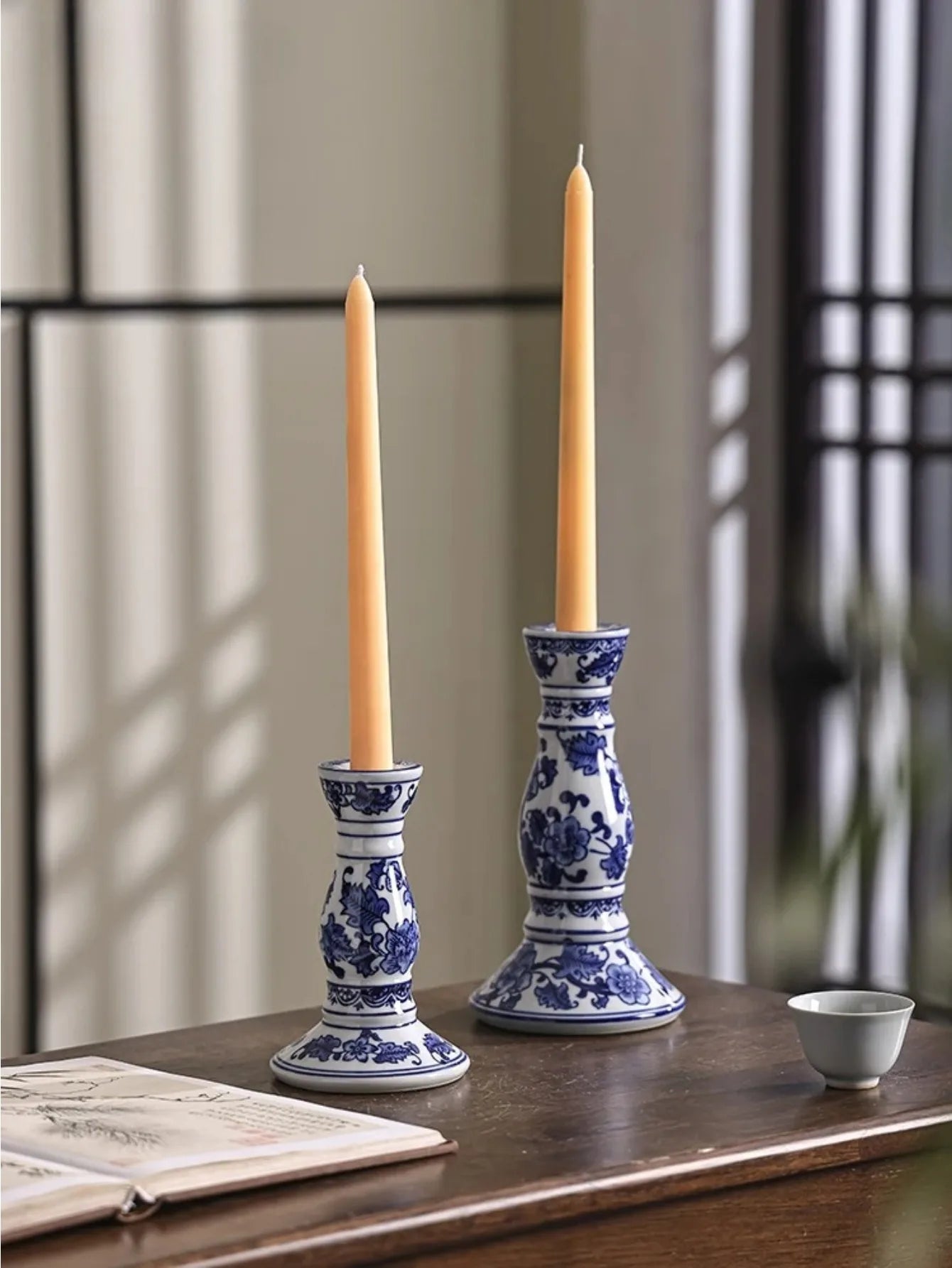 Bougeoir en porcelaine bleue et blanche Nesty - Deux bougeoirs avec bougies dorées allumées, posés sur un coffret en bois près d'une théière en terre cuite