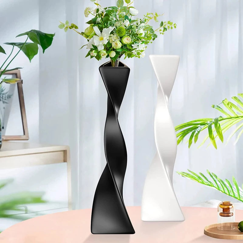 Vase céramique haut et torsadé Nesty - Coloris noir avec fleurs blanches et coloris blanc vide, sur table rose près de plantes