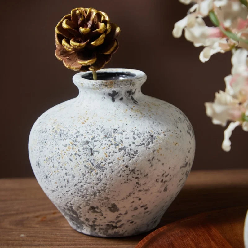 Vase en céramique fait main, esprit nostalgique Nesty, vase effet pierre tacheté garni d'une pomme de pin dorée, sur table en bois devant lampe