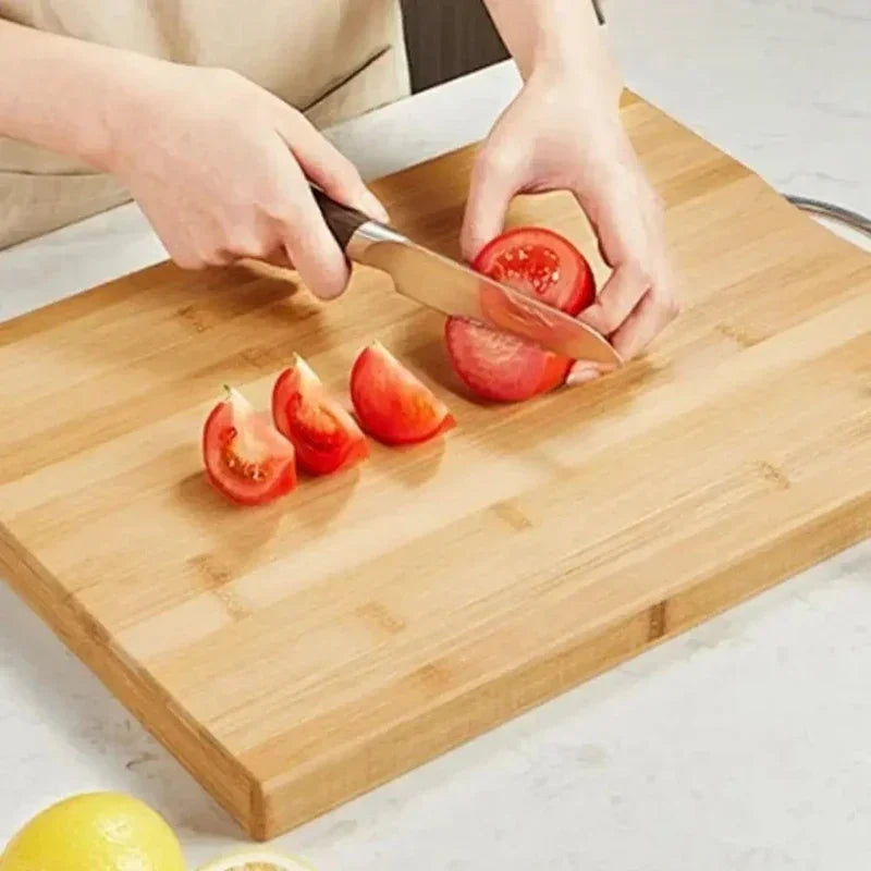 Planche à découper en bambou épaisse Nesty, mains découpant des tranches de tomate au couteau sur la planche en bambou, citrons au premier plan