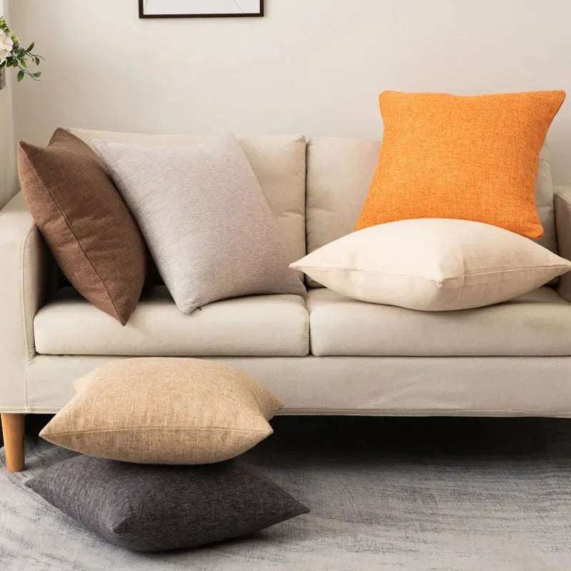 Coussin coloré avec garnissage inclus, style moderne et simple Nesty, coussins unis en lin marron, gris clair et orange sur canapé beige, deux coussins beige et anthracite posés au sol