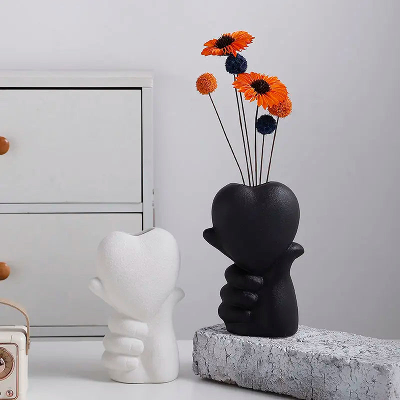 Vase en céramique forme cœur Nesty - Modèles blanc et noir, le noir sur socle en pierre avec fleurs oranges, près d'une radio vintage