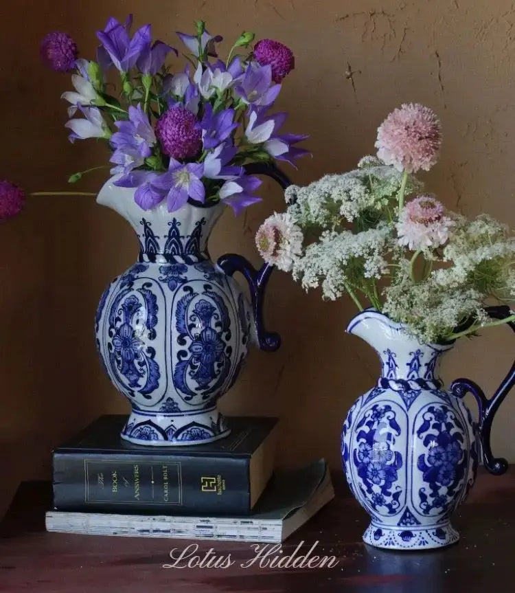 Vase en porcelaine bleu et blanc, motif ancien Nesty, deux pichets garnis de fleurs violettes et blanches, posés sur des livres