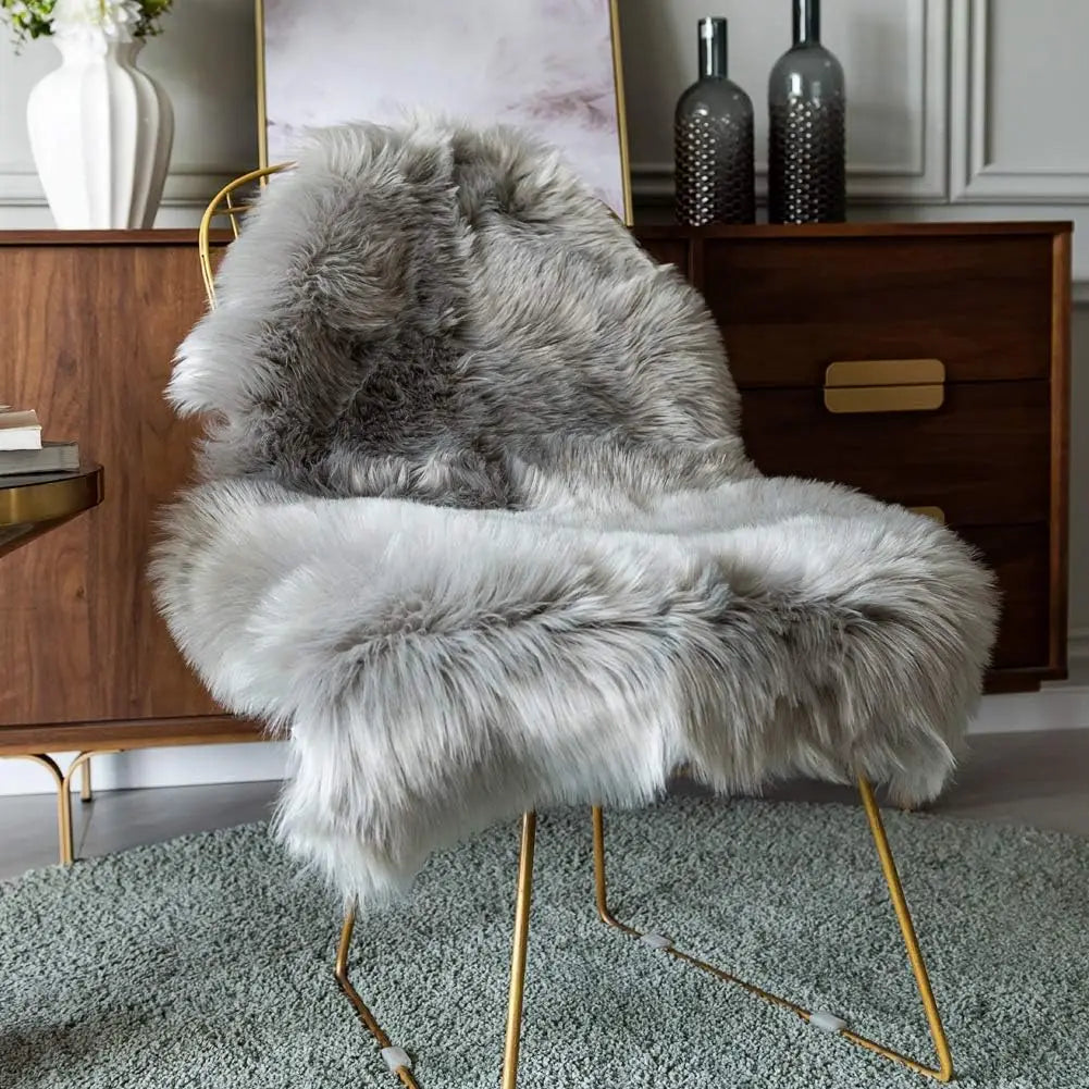 Tapis en fausse fourrure grise de forme irrégulière, drapé sur un fauteuil à pieds dorés devant une commode en bois.