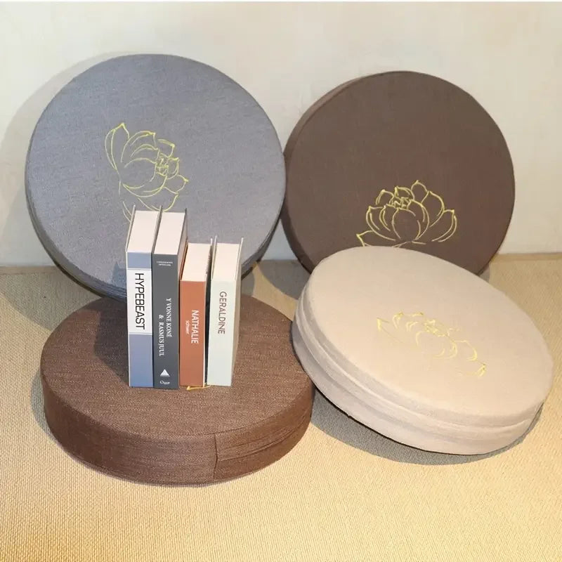 Coussin de méditation en lin, texture lotus, modèle compact Nesty, quatre coussins ronds de méditation brodés d'un lotus doré, coloris gris, marron, beige, avec pile de livres posée dessus