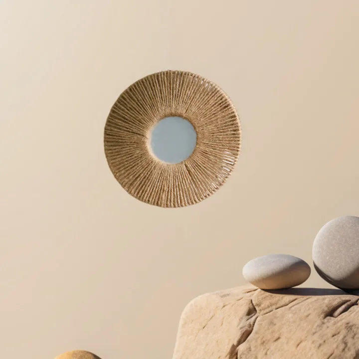 Miroir mural rond enroulé de corde de chanvre, en apesanteur au-dessus de galets sur fond beige - Nesty