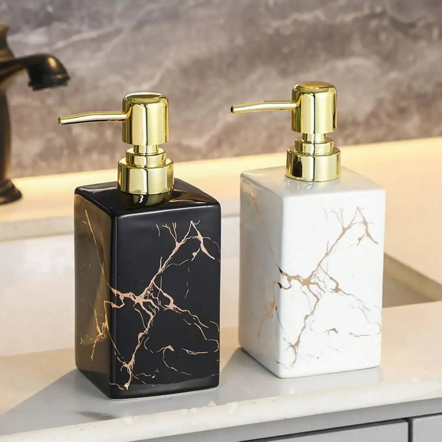 Distributeur de savon en céramique effet marbre Nesty, deux distributeurs de savon céramique effet marbre noir et blanc à veinures dorées, pompe dorée, posés sur un plan de vasque
