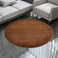 Petit tapis rond texturé marron, posé au sol dans un salon devant un canapé et un fauteuil gris.