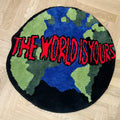 Tapis rond en acrylique — motif animalier - Nesty, tapis rond noir façon globe terrestre avec l'inscription The World Is Yours en rouge, posé sur un parquet