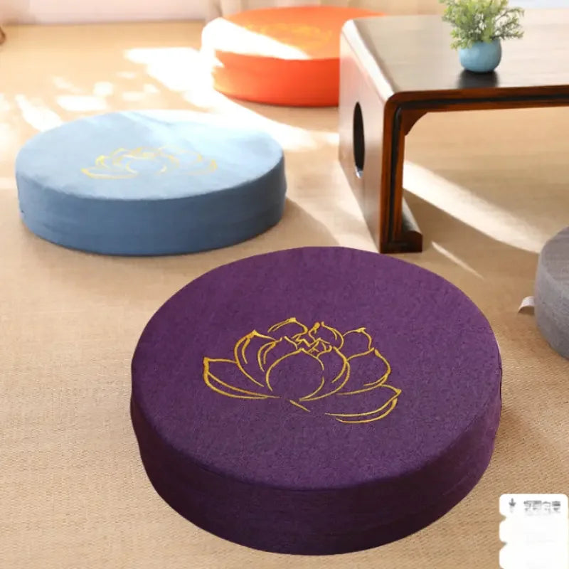 Coussin de méditation en lin, texture lotus, modèle compact Nesty, coussins ronds de méditation brodés d'un lotus doré, coloris orange, bleu ciel et violet, posés sur tapis en jonc près d'une table basse