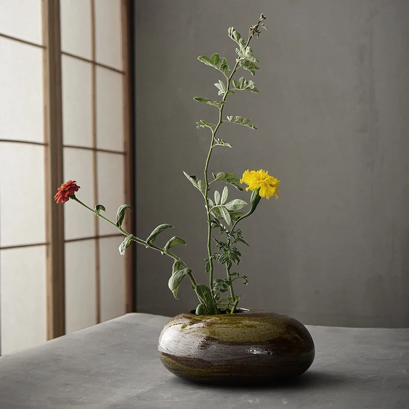 Vase en céramique brute, petit format esprit zen Nesty, vase galet en céramique brune posé sur une table, garni de fleurs rouge et jaune et de verdure