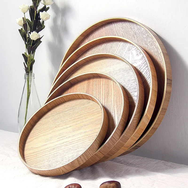 Plateau rond en bois à style japonais Nesty, plateaux de tailles étagées empilés en éventail contre un mur, avec un vase de roses blanches