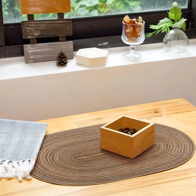 Sets de table ovales tressés Nesty - Set posé sur une table en bois avec boîte de grains de café et linge à motif