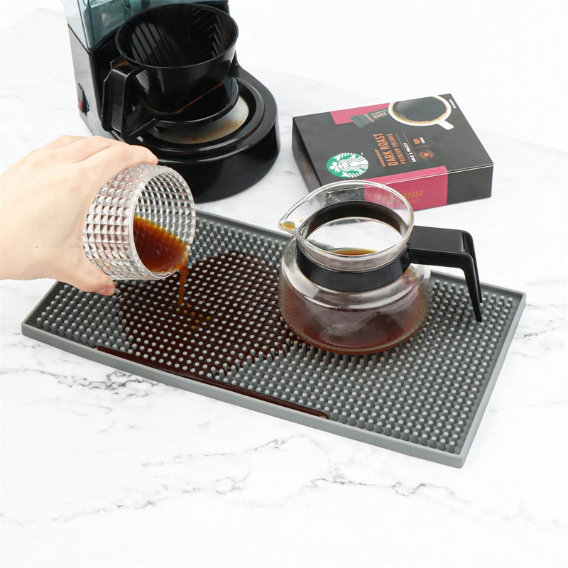 Tapis de bar en silicone gris anti-éclaboussures, café versé dessus depuis un pichet, à côté d'une cafetière et d'un paquet de café - Nesty