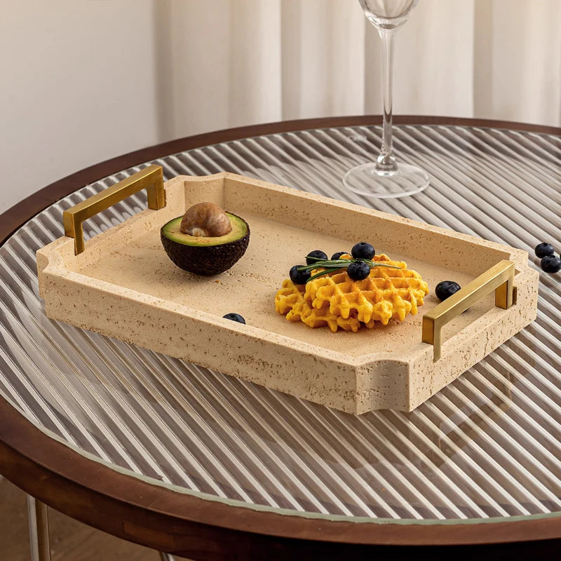 Plateau en travertin beige à poignées dorées, posé sur table ronde en verre, avec avocat coupé, gaufre et myrtilles - Nesty