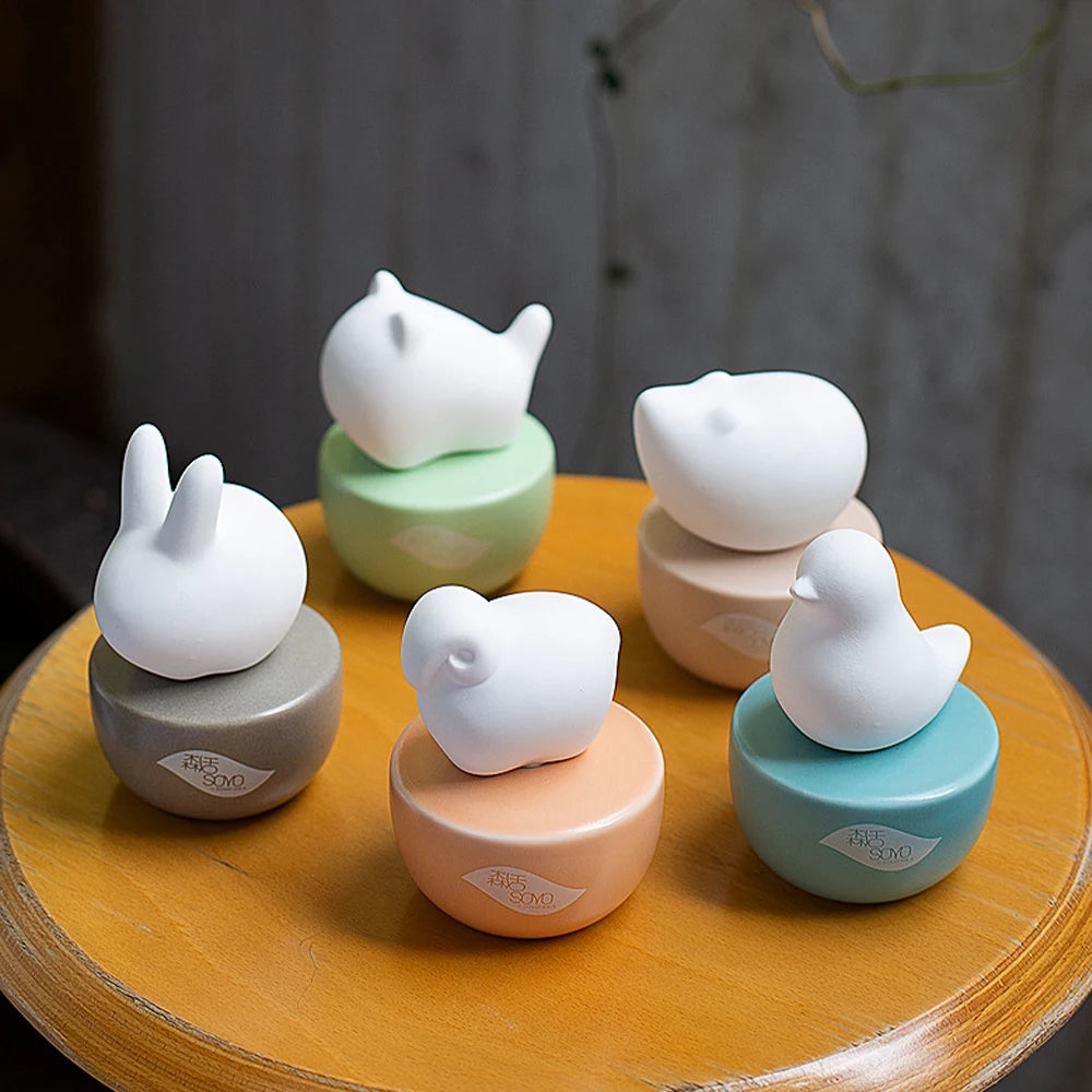 Diffuseur de parfum sans flamme forme animale Nesty - Cinq figurines lapin et oiseaux sur socles pastel, posées sur table en bois