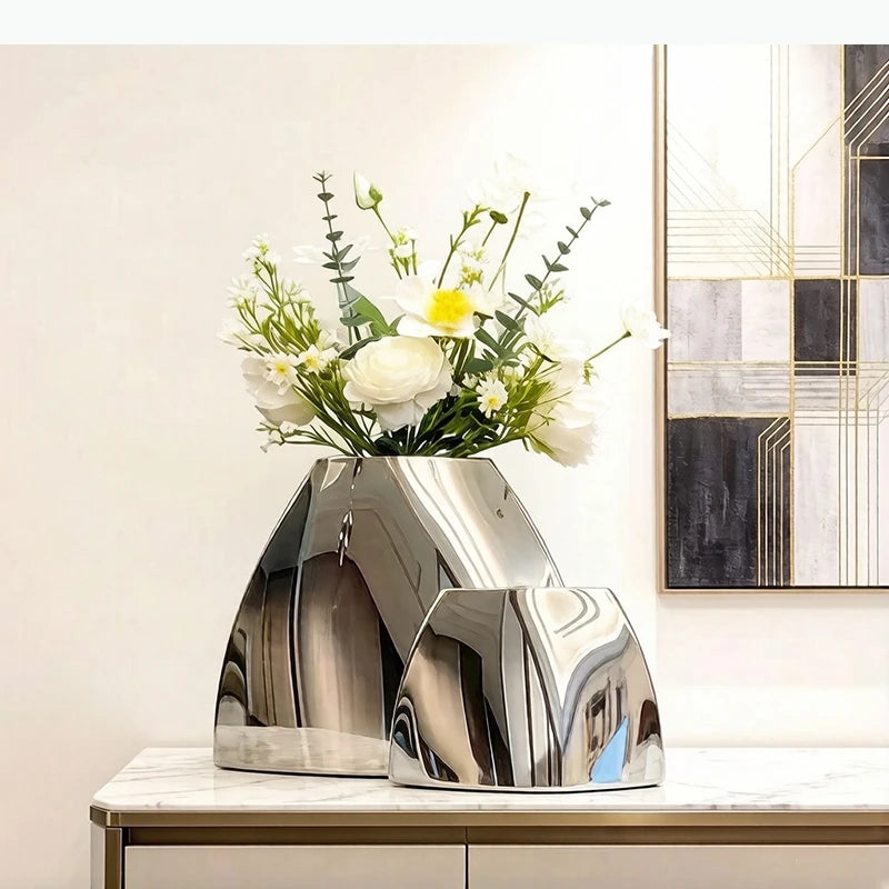 Vase arc en métal argenté — silhouette minimaliste - Nesty - Deux tailles en finition miroir argentée avec bouquet de fleurs blanches et jaunes, sur console marbre près d'un tableau géométrique