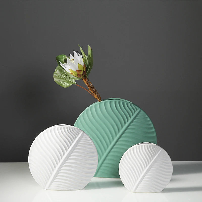 Vase céramique de style européen, motif feuille - Nesty - Grand modèle vert sauge avec une fleur blanche exotique, petits modèles blanc et vert clair côte à côte, fond gris foncé