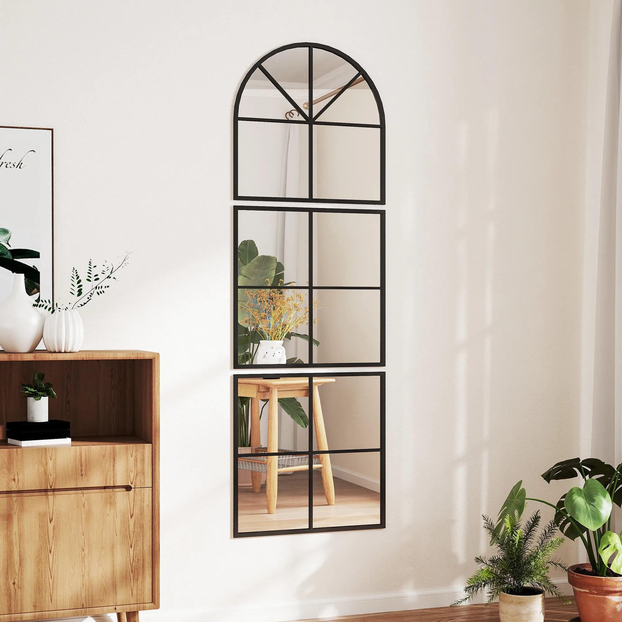 Miroir cintré segmenté Nesty - Cadre métal noir, accroché sur un mur beige au-dessus d'une commode avec vases et livres