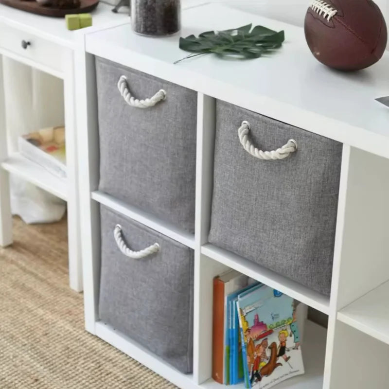Boîte de rangement pliable en lin pour vêtements Nesty, boîtes grises insérées dans un meuble étagère cubique blanc avec livres et ballon de football