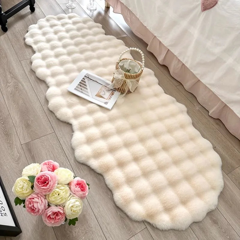 Tapis ovale en fausse fourrure douce Nesty - Chevet, coloris ivoire posé au pied d'un lit avec fleurs et panier