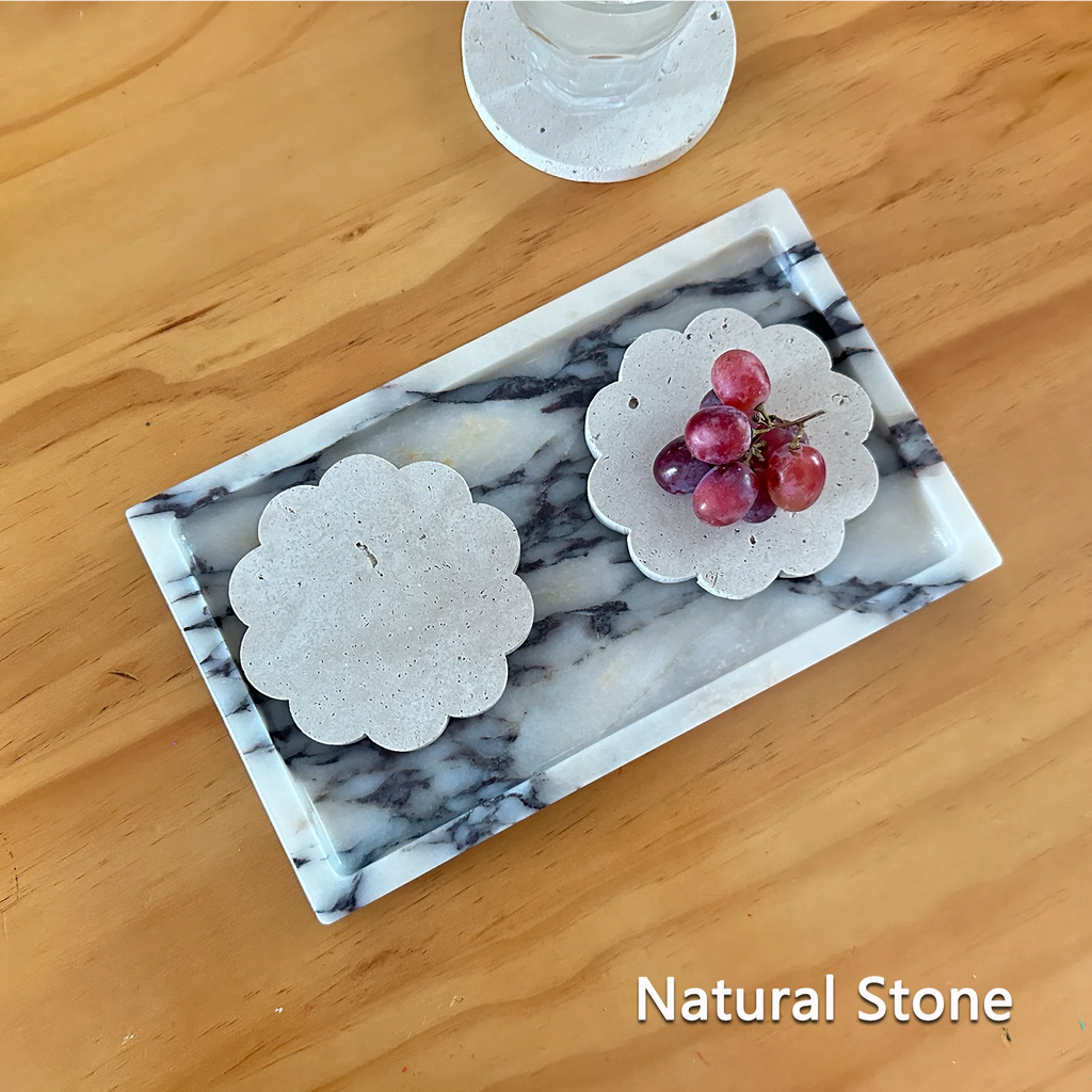 Deux dessous de verre en travertin, bord festonné, sur un plateau en marbre avec grappe de raisin, texte 'Natural Stone' - Nesty