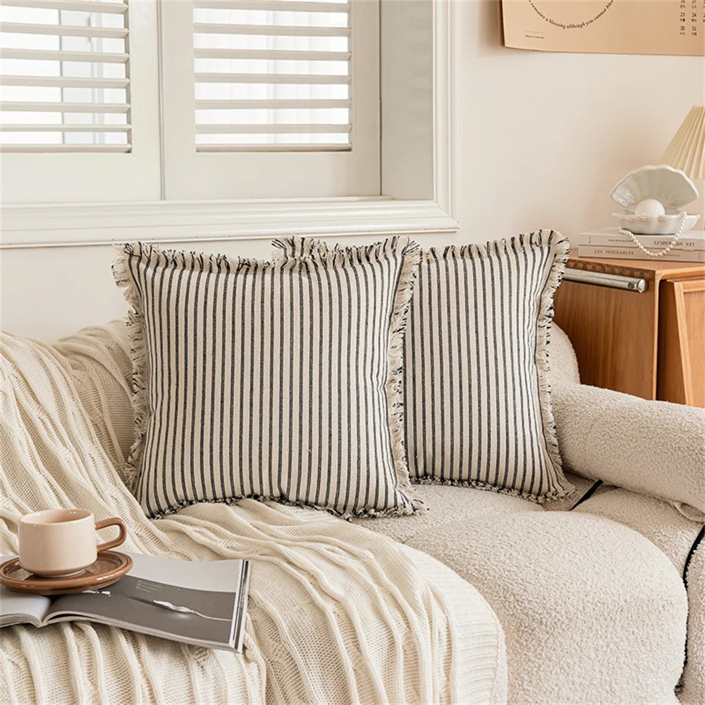 Housse de coussin en lin à rayures, plusieurs formats disponibles Nesty, deux housses de coussin carrées à rayures noir et blanc avec bordures à franges, posées sur canapé écru bouclette