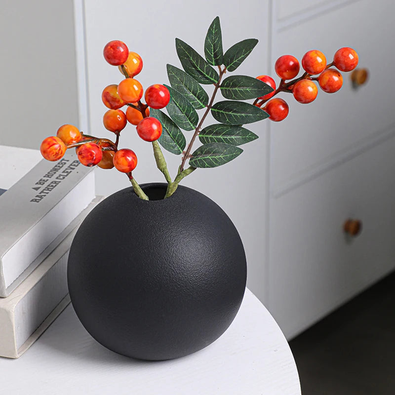Vase céramique boule bicolore noir et blanc - Nesty - Vase boule noir garni de branches de baies oranges et de feuillage vert, posé sur des livres empilés près d'une commode