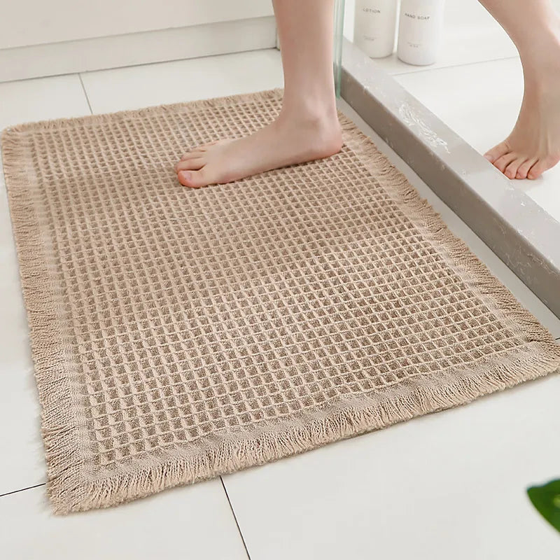 Tapis de bain gaufré à pompons Nesty - Tapis beige texture gaufrée à franges, posé devant une douche