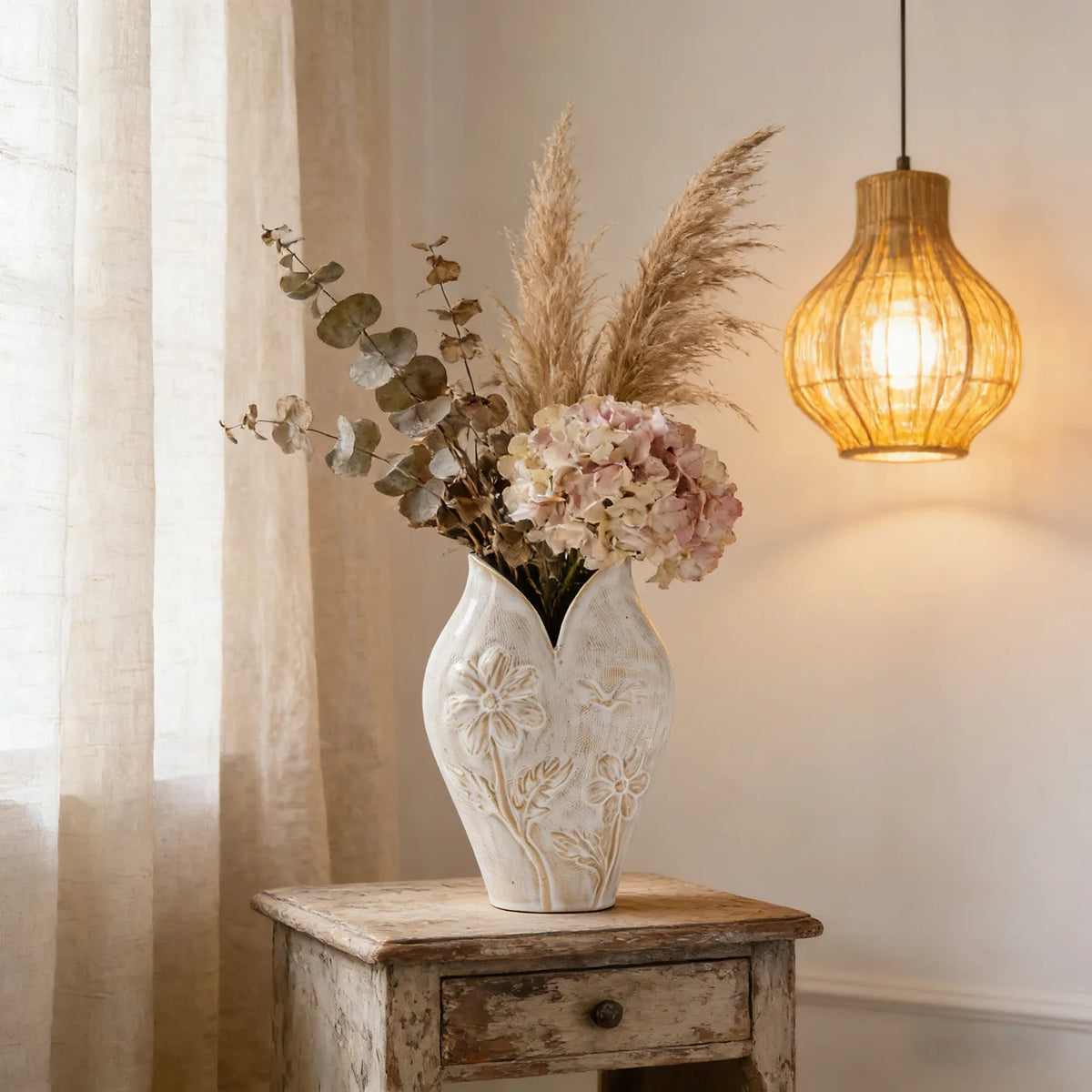 Vase en céramique forme poisson, esprit wabi-sabi Nesty, vase blanc à relief floral gravé, garni de pampa, hortensia séché et eucalyptus, sur table ancienne près d'une suspension en rotin