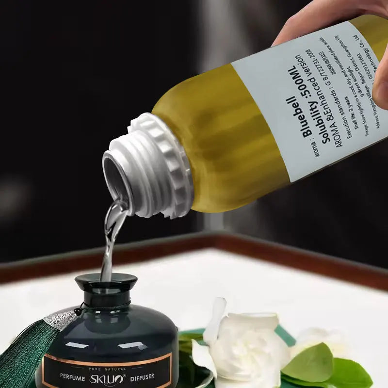 Recharge huile parfumée pour diffuseur Nesty - Versement du parfum liquide dans un diffuseur à bâtonnets près de fleurs blanches