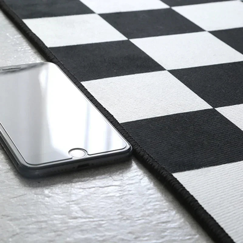 Gros plan sur le bord d'un tapis à motif damier noir et blanc posé sur une table, avec un smartphone à côté pour montrer l'échelle.