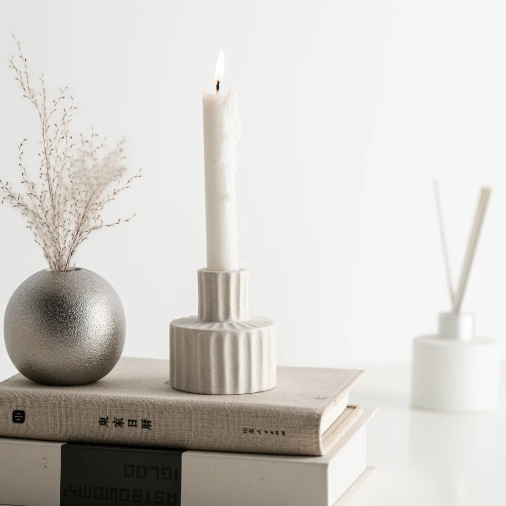 Bougeoir céramique nordique godronné blanc, bougie blanche allumée, sur pile de livres avec vase en métal argenté et bâtons parfumés - Nesty