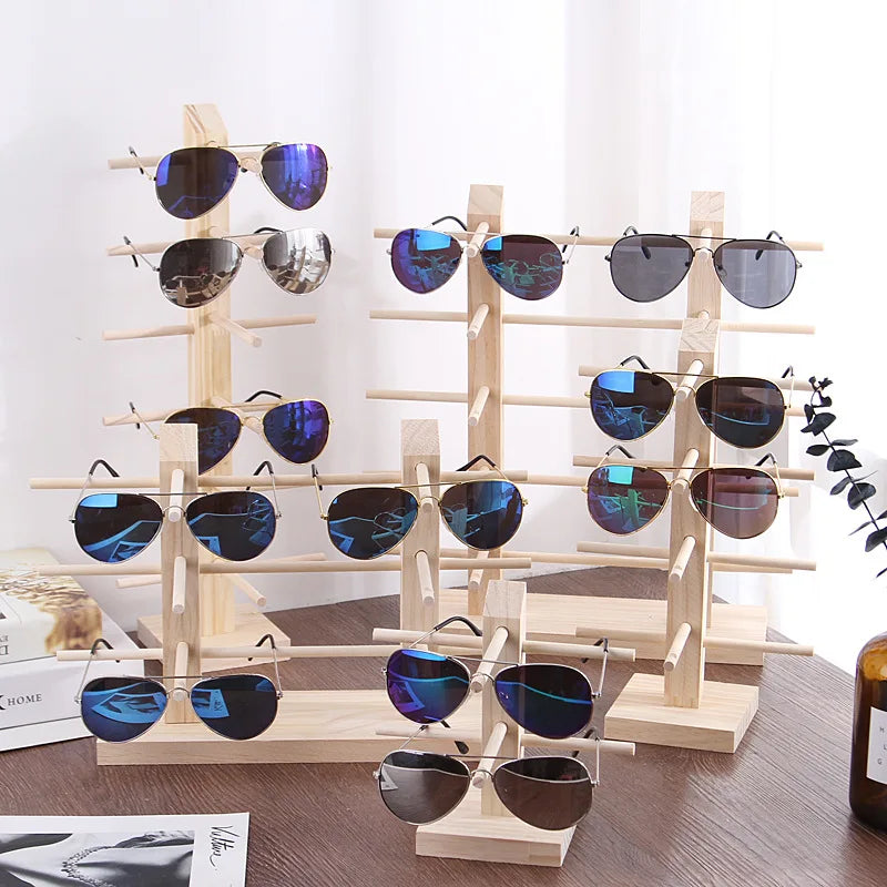 Présentoir à lunettes en bois à plusieurs niveaux Nesty, plusieurs présentoirs en bois clair garnis de lunettes de soleil sur une table sombre