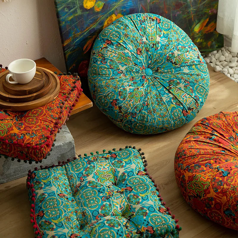 Gros coussin de sol en coton et lin épais, esprit marocain Nesty, coussin de sol rond turquoise à motif marocain et coussins carrés orange et turquoise à pompons, sur parquet devant un tableau
