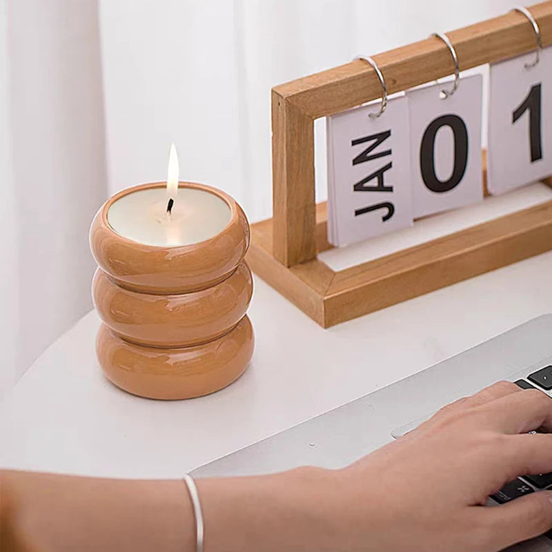 Bougeoir cylindrique en céramique blanche Nesty - Bougeoir orange empilé en anneaux avec bougie allumée, posé sur un bureau près d'un calendrier en bois