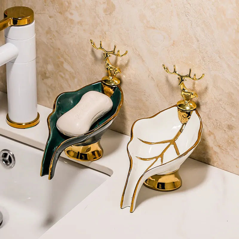 Duo de porte-savons en céramique forme feuille avec figurine de cerf dorée, coloris vert avec savon et blanc, près d'un robinet et d'une vasque - Nesty