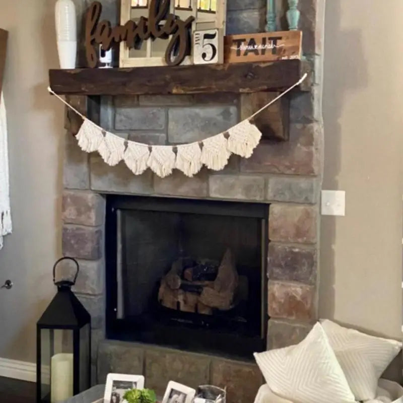 Tenture macramé à franges à tissage bohème Nesty, guirlande accrochée sur une cheminée en pierre avec décorations murales et lanterne