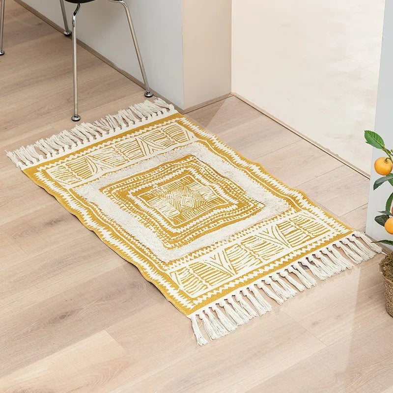 Tapis noué main à franges — motif géométrique - Nesty, variante jaune moutarde et écru à motifs géométriques concentriques, franges, posée près d'une chaise