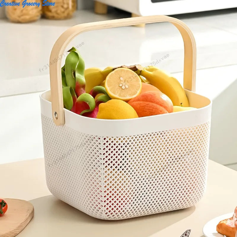 Panier de rangement ajouré en plastique avec poignée bois Nesty, coloris blanc garni de fruits (banane, citron, pomme), poignée arquée en bois, sur plan de travail