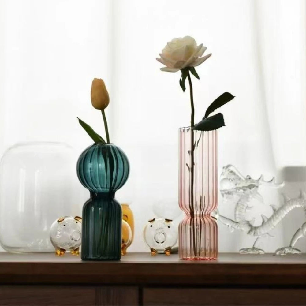 Vase en verre strié coloré, esprit scandinave Nesty, vase bleu canard forme boule garni d'une tulipe jaune et vase rose garni d'une rose blanche, figurines en verre à côté