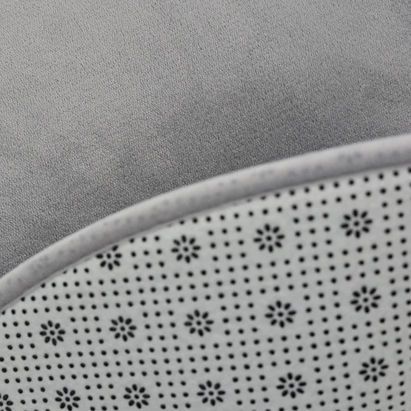 Gros plan sur le bord d'un tapis rond en velours gris, montrant l'envers antidérapant à motif de pois blancs.