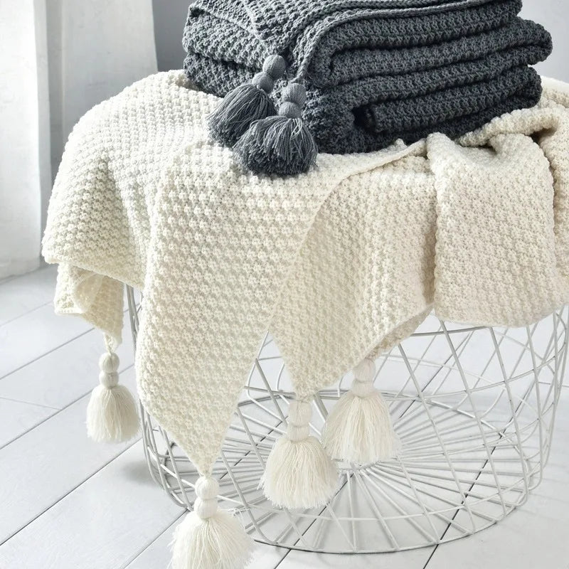 Plaid tricoté uni gaufré Nesty - Coloris blanc cassé et gris anthracite empilés sur panier en fil métallique, pompons visibles