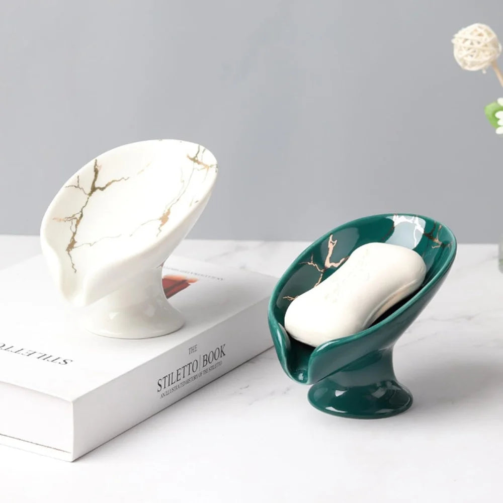 Duo de porte-savons en céramique forme feuille effet marbre, coloris blanc doré et vert émeraude doré, posés sur un livre - Nesty