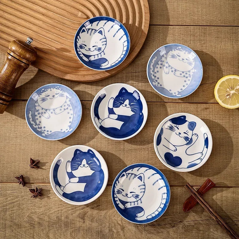 Coupelles en céramique à motif chat porte-bonheur Nesty, sept coupelles à motifs de chats variés, vue de dessus sur une table en bois