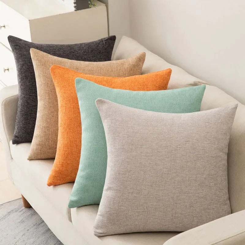 Coussin coloré avec garnissage inclus, style moderne et simple Nesty, cinq coussins unis en lin, coloris anthracite, camel, orange, vert menthe et gris clair, alignés sur canapé beige